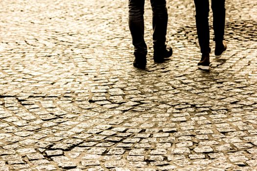 Two people walking on a textured cobblestone street, capturing motion and pattern.
