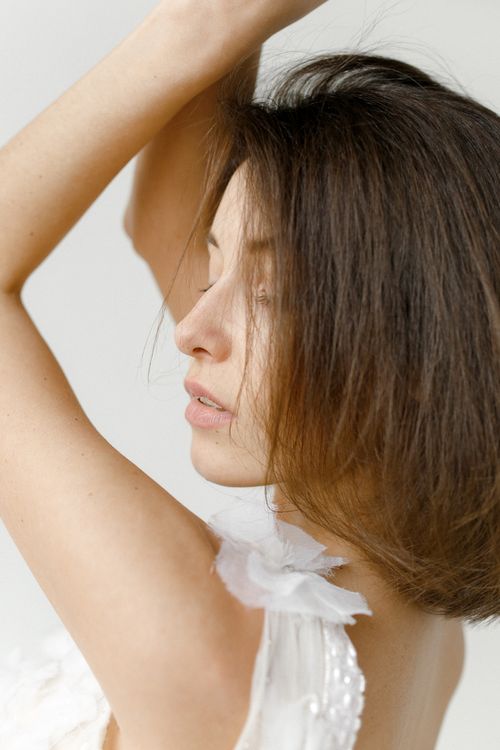 Free Close-up of a woman in a sleeveless dress with eyes closed and arms raised, evoking a serene mood. Stock Photo