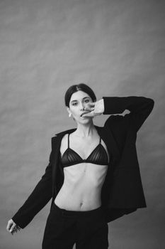Elegant black-and-white studio portrait of a fashionable woman posing in a black coat and bra.