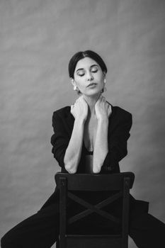 Monochrome studio portrait of a woman sitting on a chair with eyes closed, exuding elegance and calm.