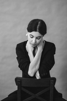 Monochrome portrait of a woman in a black blazer sitting on a chair, hands crossed over her chest.