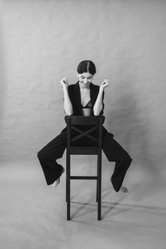 A stylish black and white portrait of a woman confidently posing on a bar stool in a studio. Grayscale elegance.