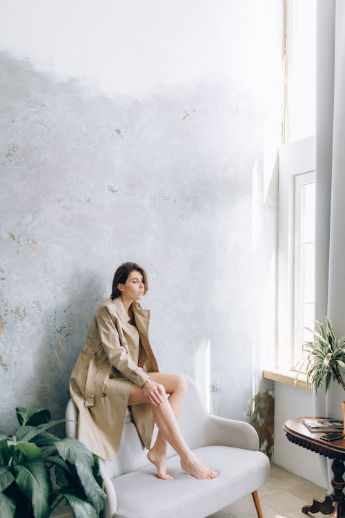 Model in a Long Beige Coat Sitting on the Backrest of a Sofa