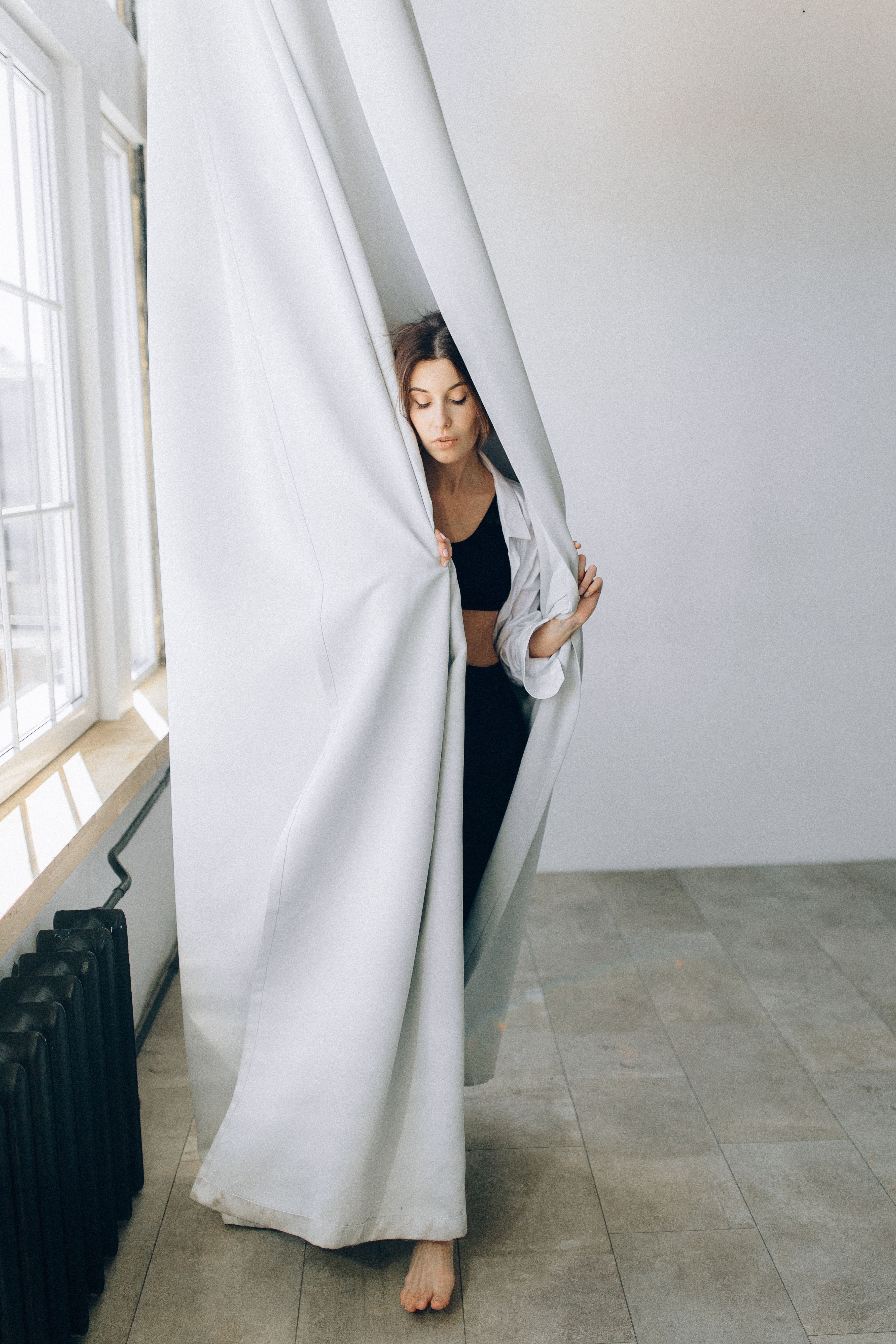一位女子赤脚闭眼，站在室内白色窗帘前的艺术肖像