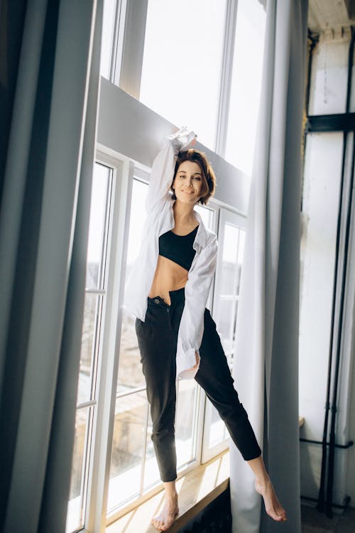 Woman in Black and White Crop Top and Black Pants Standing Beside Window