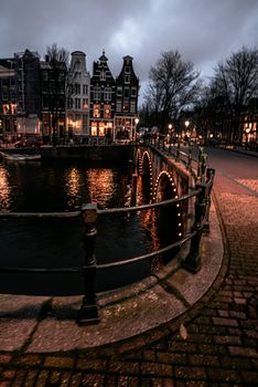 Night view of a canal in Amsterdam with lit bridge and historic buildings in the background.