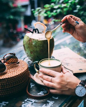 Person enjoying creamy coffee with coconut outdoors, evoking relaxation and a tropical vibe.