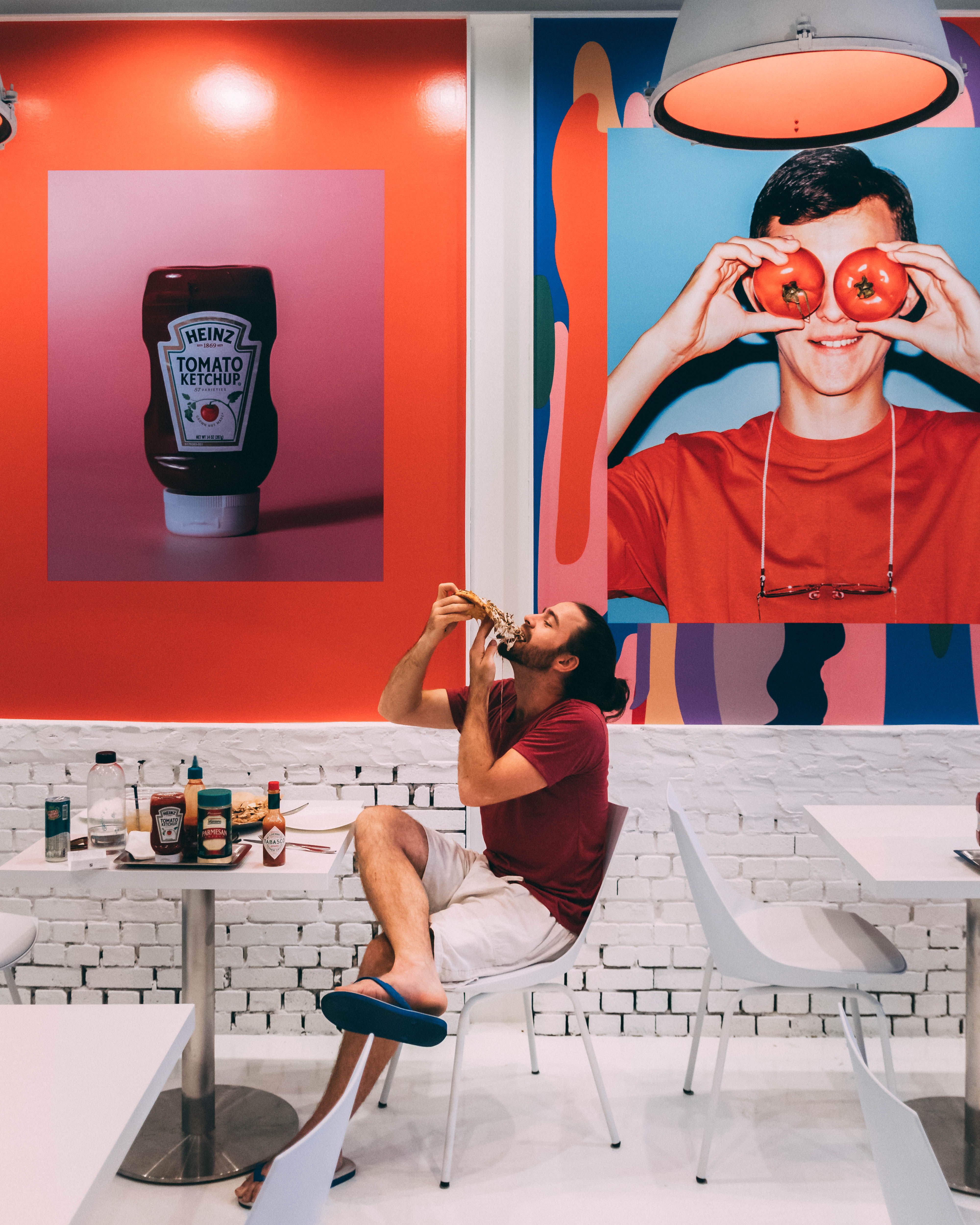 A person enjoys pizza in a trendy cafe with vibrant artwork on the walls.