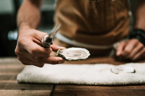 Free Close-up of chef's hand shucking an oyster on a wooden table in the kitchen. Stock Photo