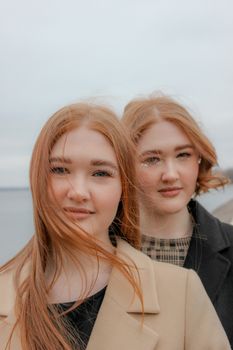 在一个大风的日子里，两位红发年轻女子微笑着在海边摆姿势的肖像