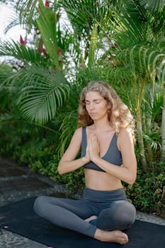 Peaceful woman practicing yoga outdoors, sitting on a mat in serene surroundings.