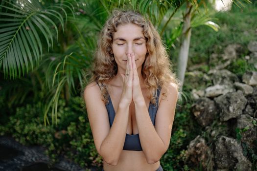 Peaceful woman practicing meditation with praying hands amidst lush greenery.
