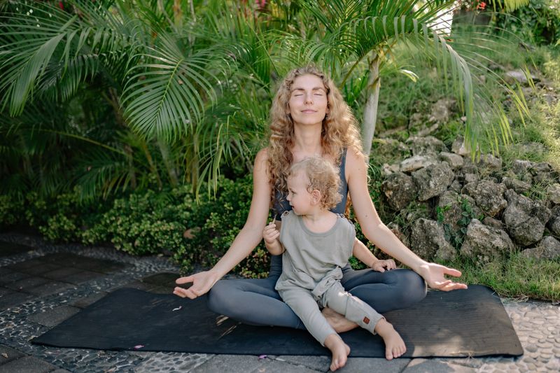 A mother meditating outdoors with her toddler on her lap