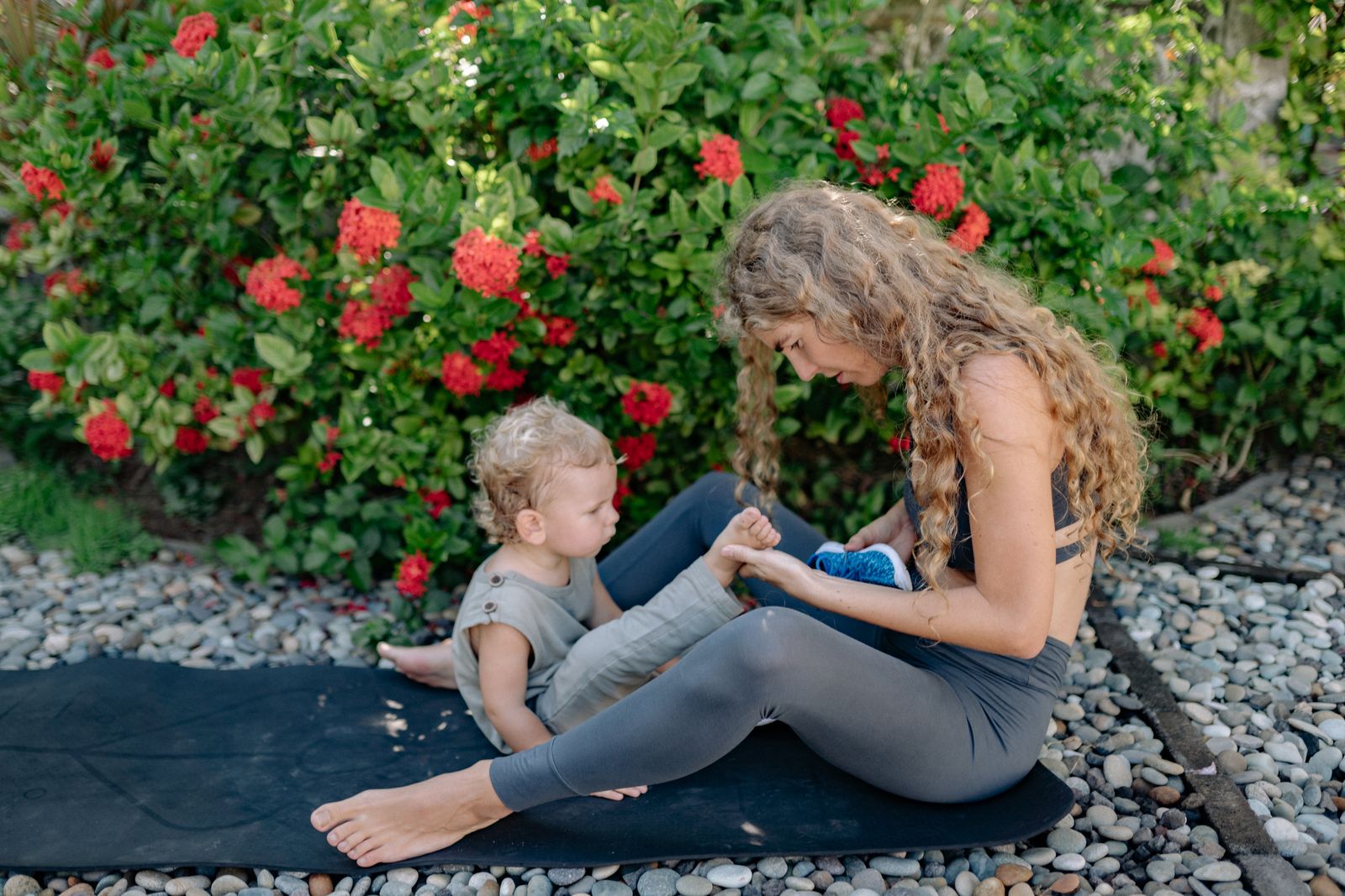 New mother resting with her baby on a yoga mat in a sunny garden after practicing postpartum yoga