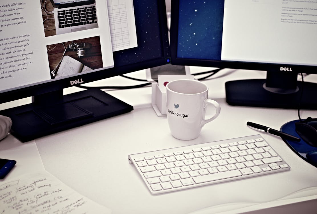 Free White Ceramic Mug Between Apple Magic Keyboard and Two Flat Screen Computer Monitors Stock Photo