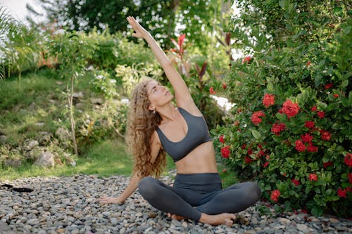 Slender lady raising hand while practicing yoga in colorful park