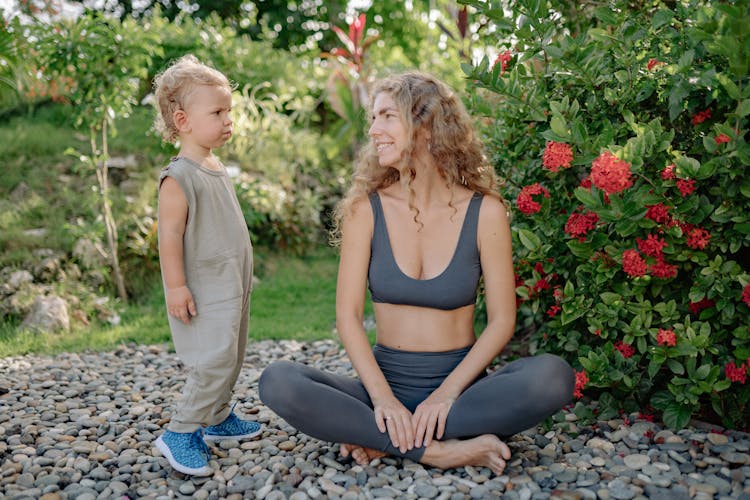 Mother With Charming Child Practicing Yoga In Bright Garden