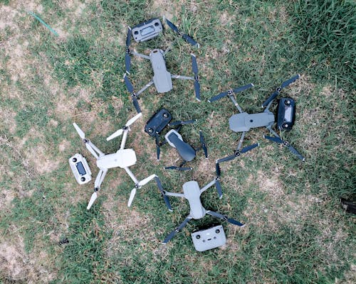 Overhead view of collection of contemporary unmanned aerial vehicles with remote controllers on grass meadow in daylight