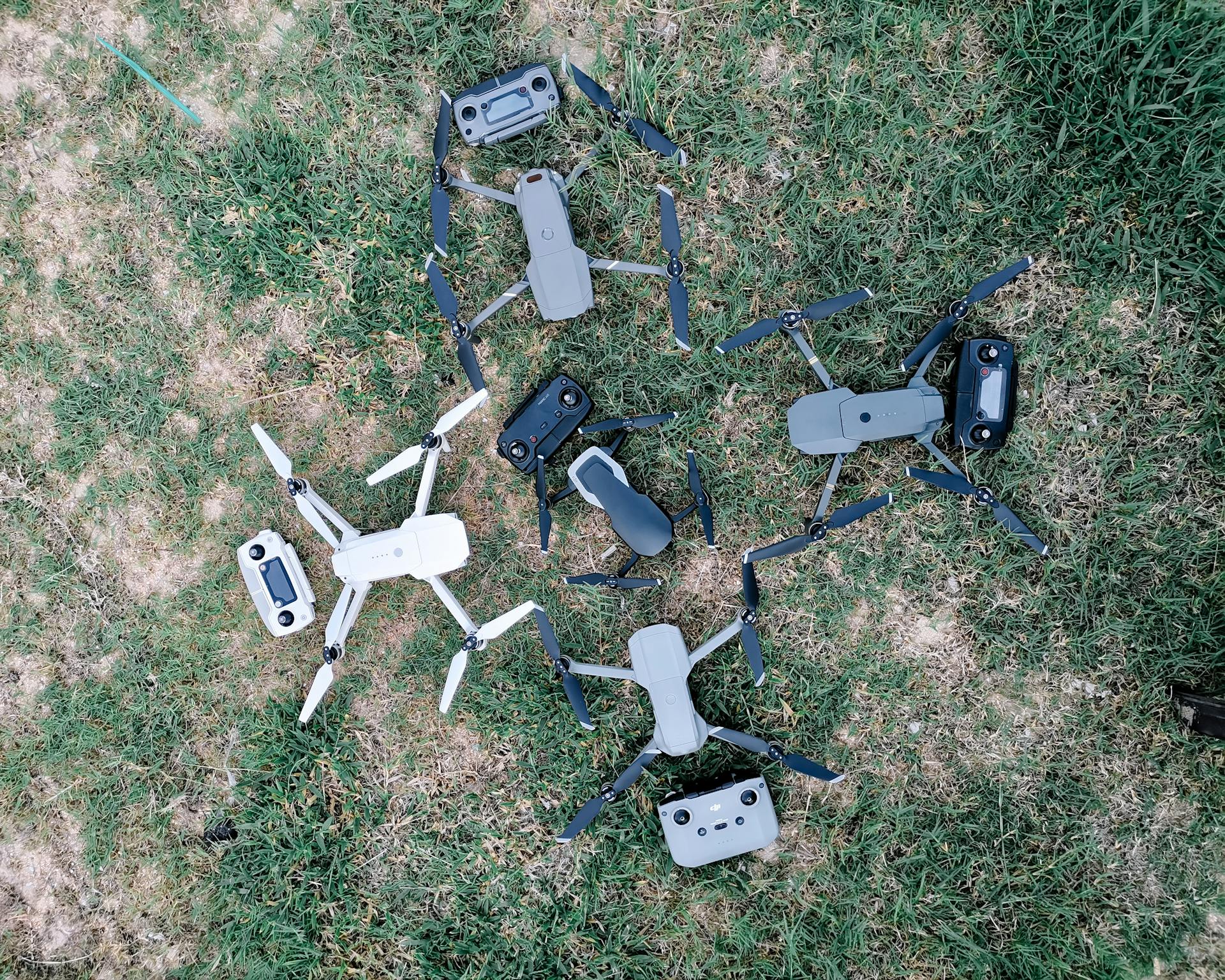 Overhead view of collection of contemporary unmanned aerial vehicles with remote controllers on grass meadow in daylight