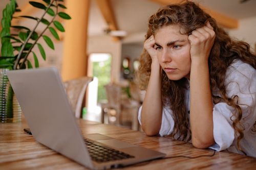 Free A woman with curly hair intensely focusing on her laptop indoors with plants and natural lighting. Stock Photo
