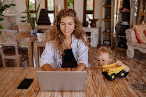 A Mother Using Laptop and Boy Playing a Toy