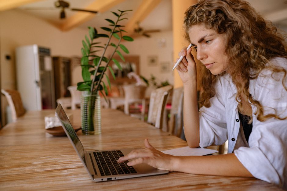 Perplexity AI vs ChatGPT: Research and Fact-Checking Workflow (2024) Focused woman with curly hair using laptop at home table, multitasking and working remotely.
