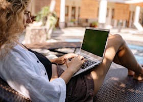Relaxing professional woman working on a laptop outdoors by the poolside.