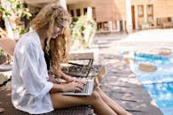Blonde Woman Sitting with Laptop and Working by Swimming Pool