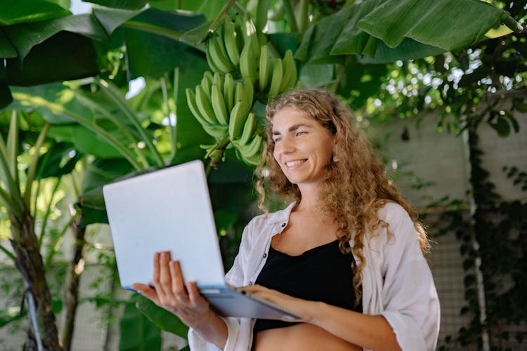 Photo Of A Woman With A Laptop, Standing Against A Banana Plant