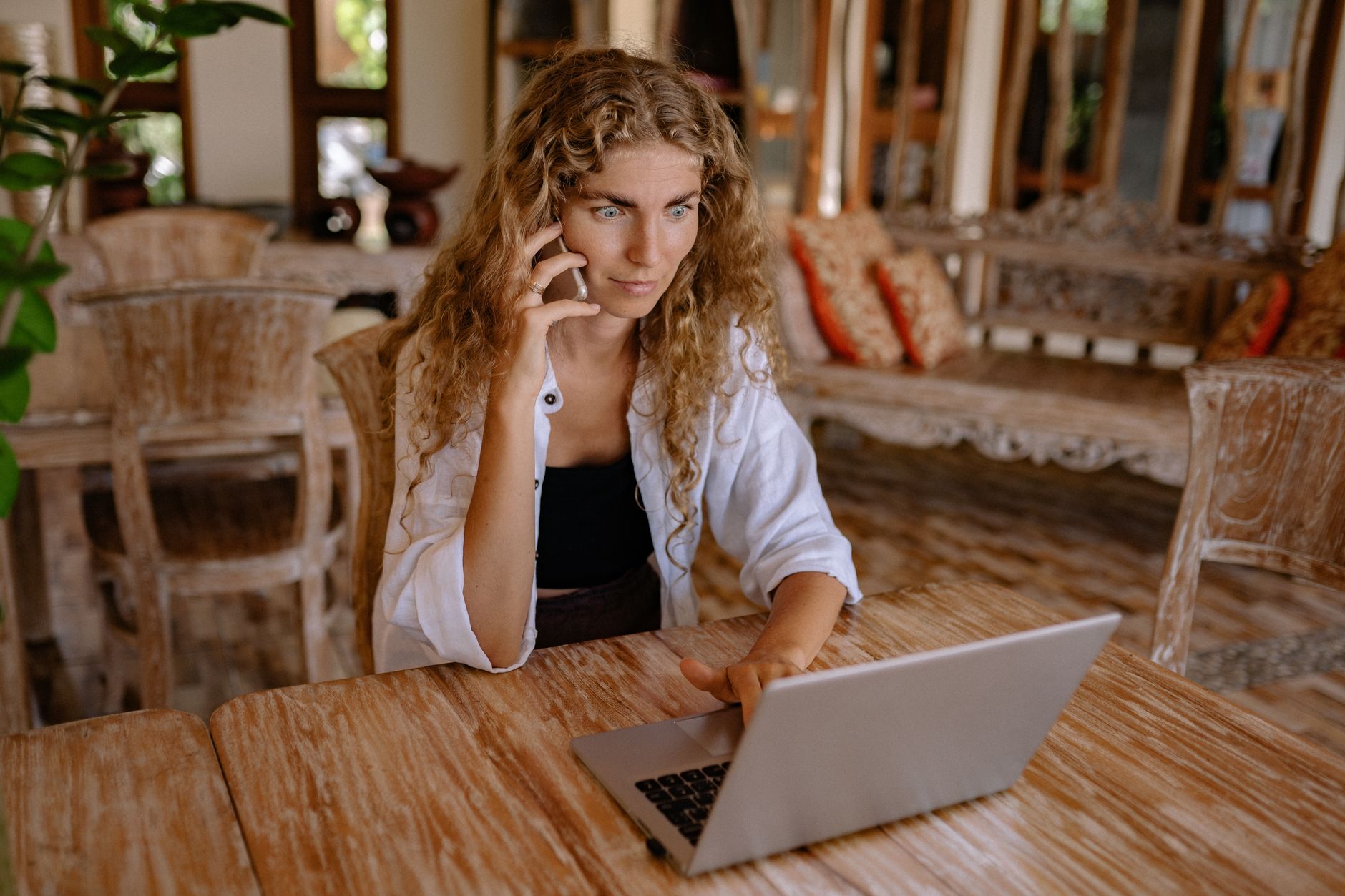 Woman working remotely on a laptop while talking on phone, capturing freelance lifestyle.