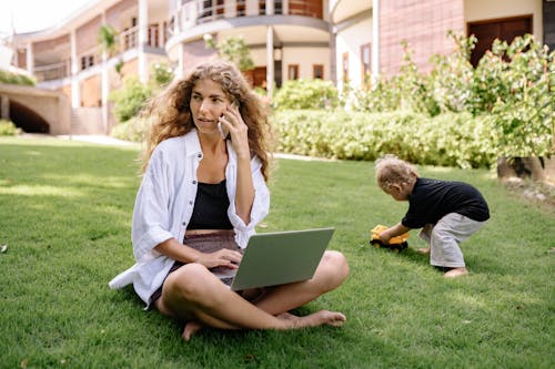 Free Photo of Woman Using Silver Laptop With Her Child Playing on Grass Field Stock Photo
