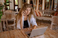 一名女子在舒适的室内环境中，坐在木桌前用笔记本电脑打电话