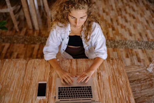 Woman typing on laptop with smartphone nearby, engaged in remote work.