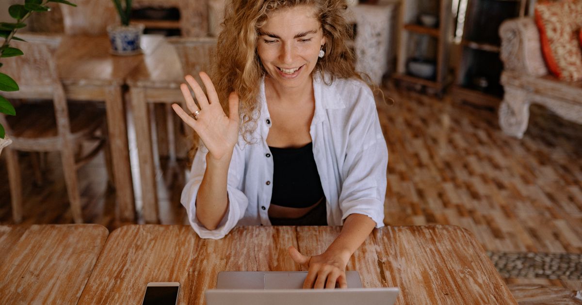 A smiling woman waving hello during a video call on her laptop