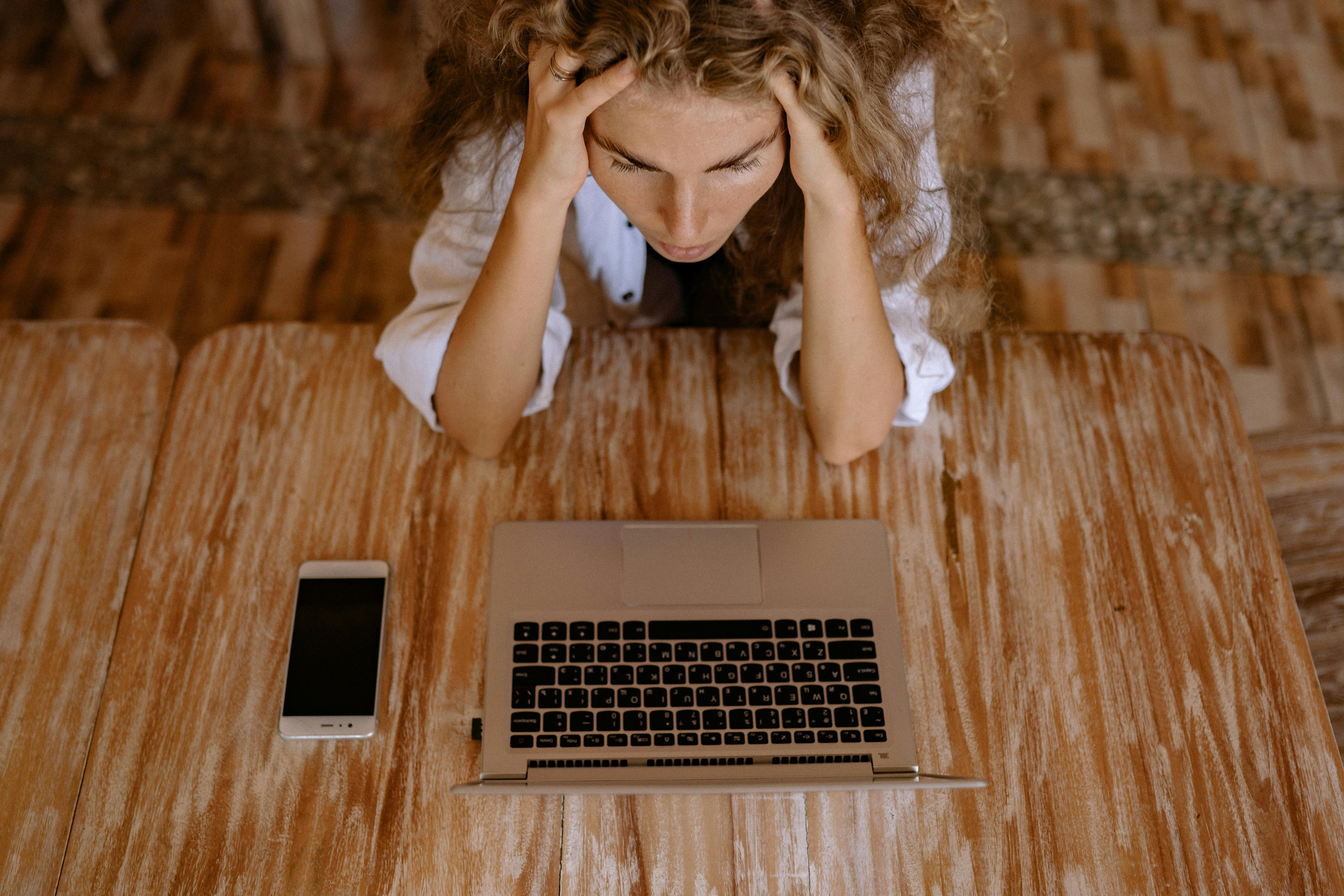 high angle photo of woman looking upset in front of silver laptop