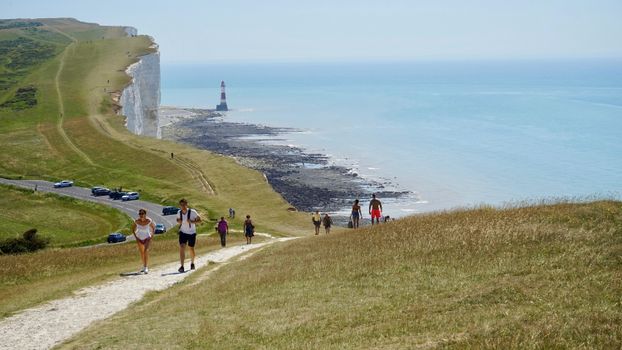 People hiking along coastal cliffs with a lighthouse in view.