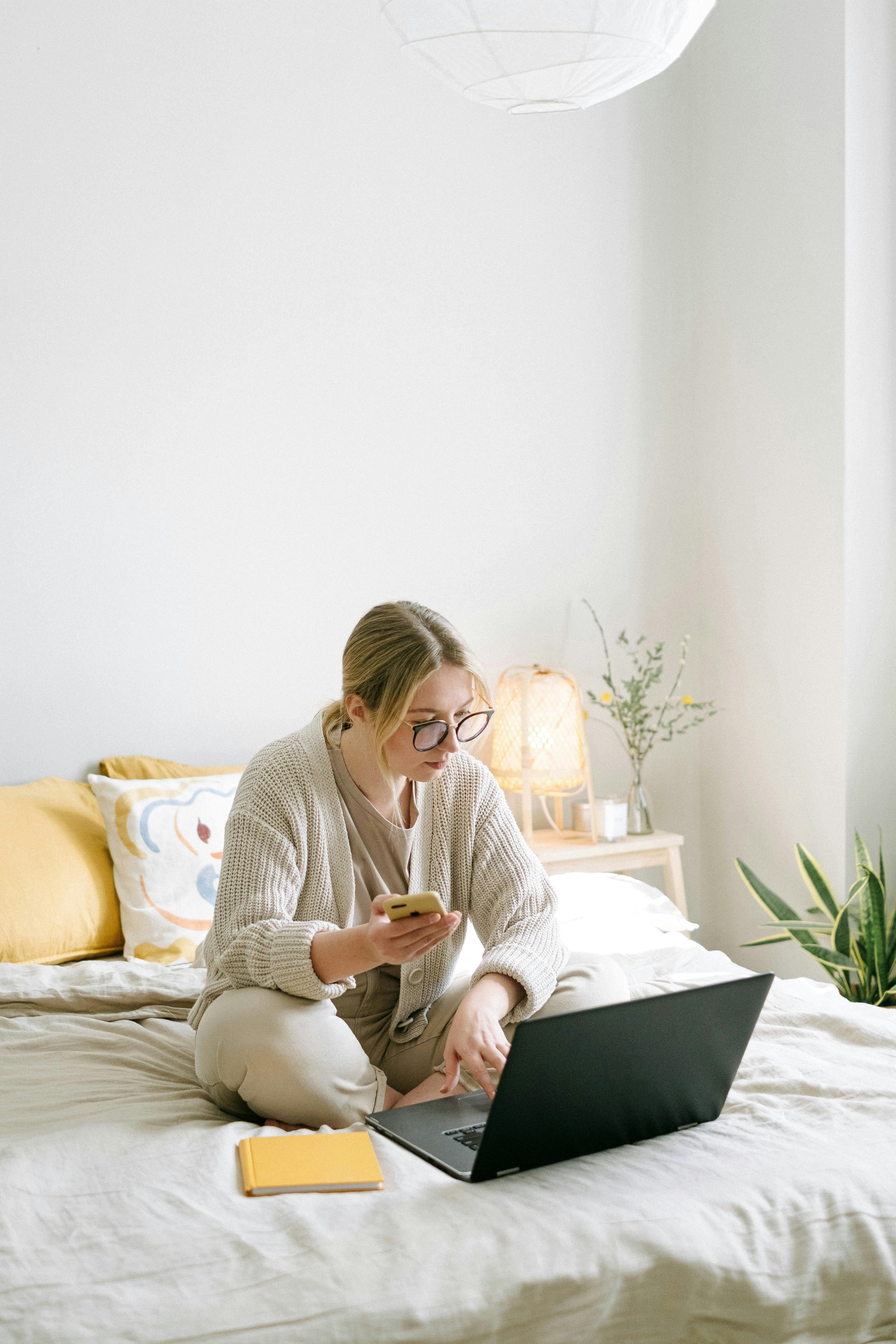 photo of woman sitting on bed while using black laptop
