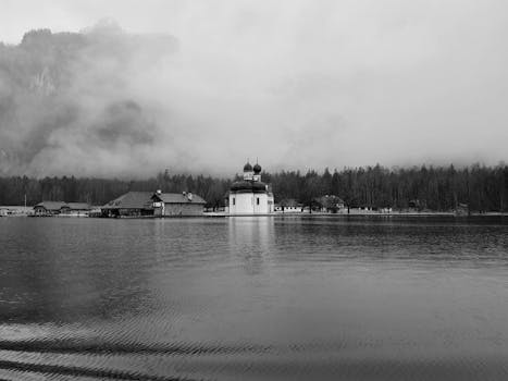 Black and white scenery of old St Bartholomew Church built on pond coast in peaceful countryside area
