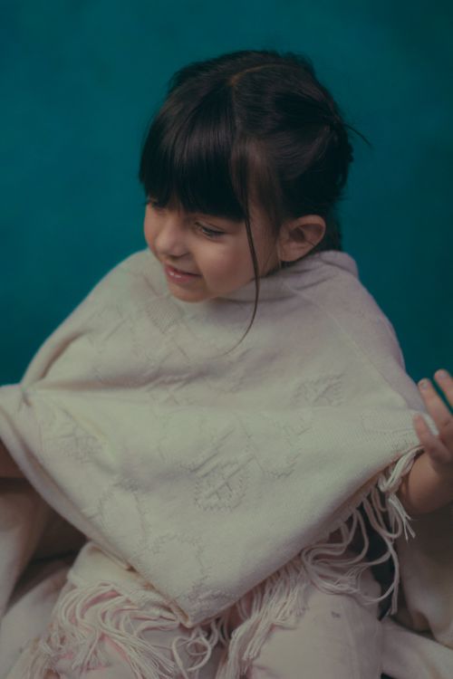 Free Charming portrait of a smiling little girl wrapped in a warm scarf, gesticulating playfully indoors. Stock Photo