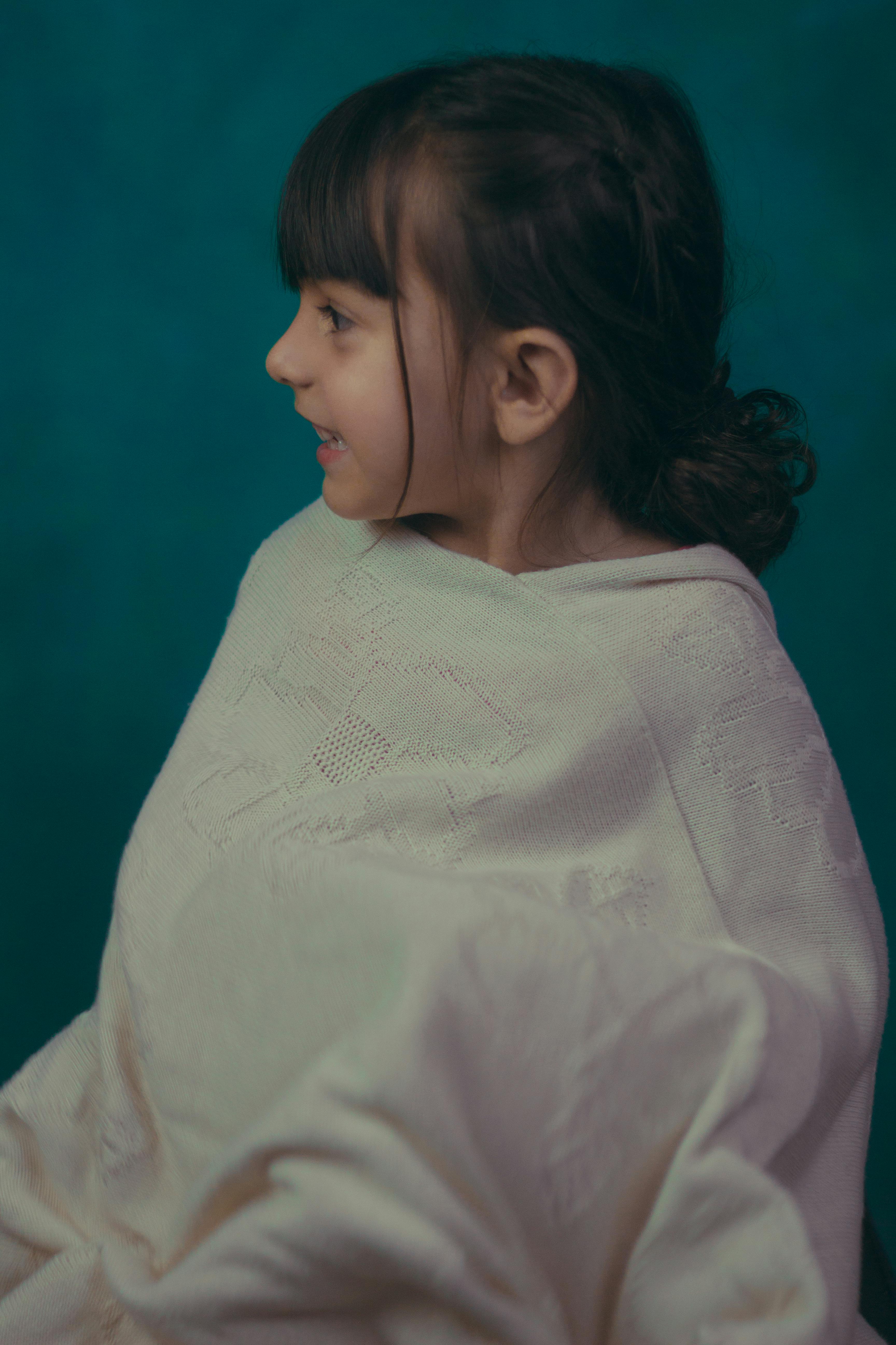 Charming portrait of a young girl smiling while wrapped in an oversized sweater against a teal background.