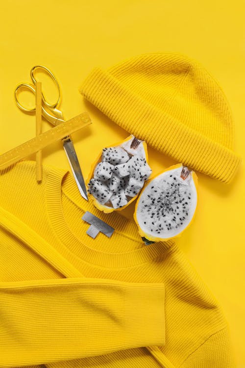 Top view of yellow hat sweater scissors and fruit united in excitement and bold art composition