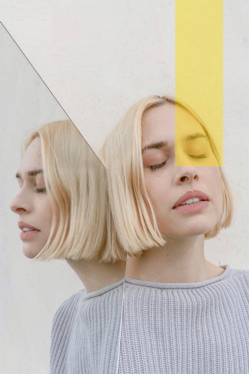 Pensive young woman with closed eyes reflecting in mirror