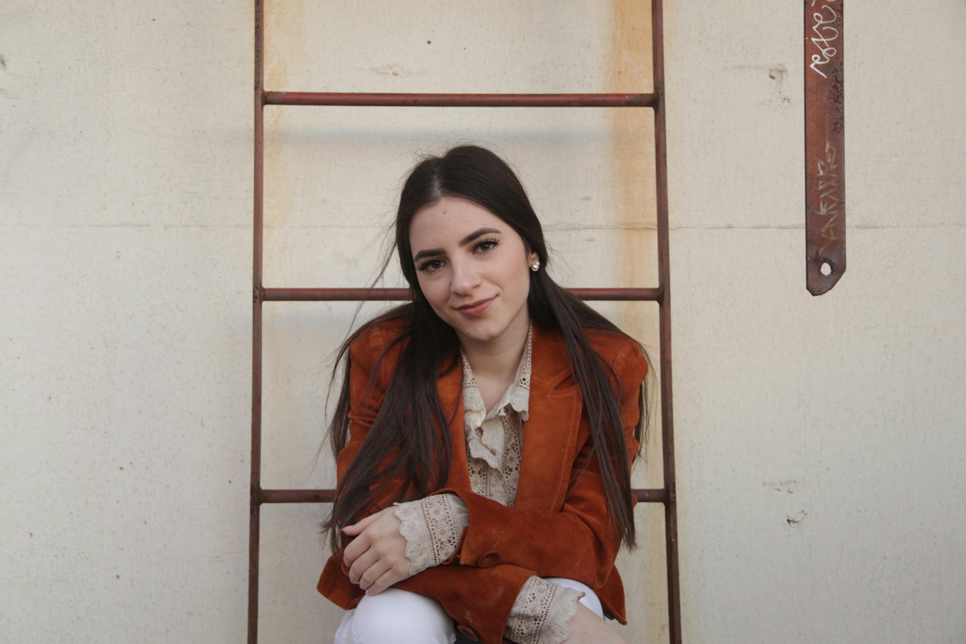 A fashionable woman in a brown blazer poses by a rustic ladder in Austin, Texas.