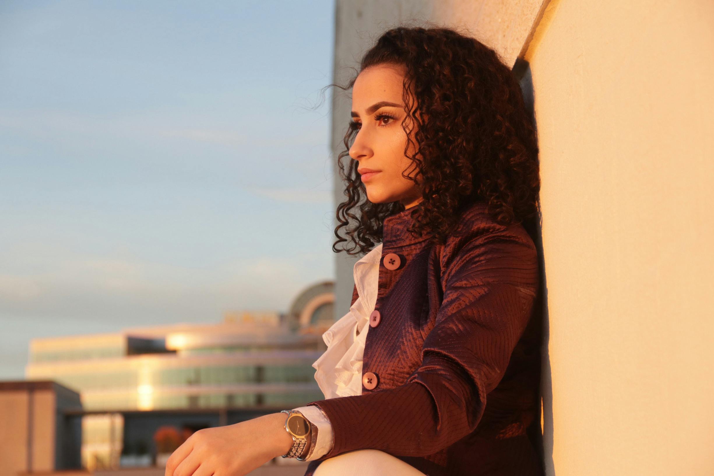 A stylish woman with curly hair posing against a wall at sunset in Austin, Texas.