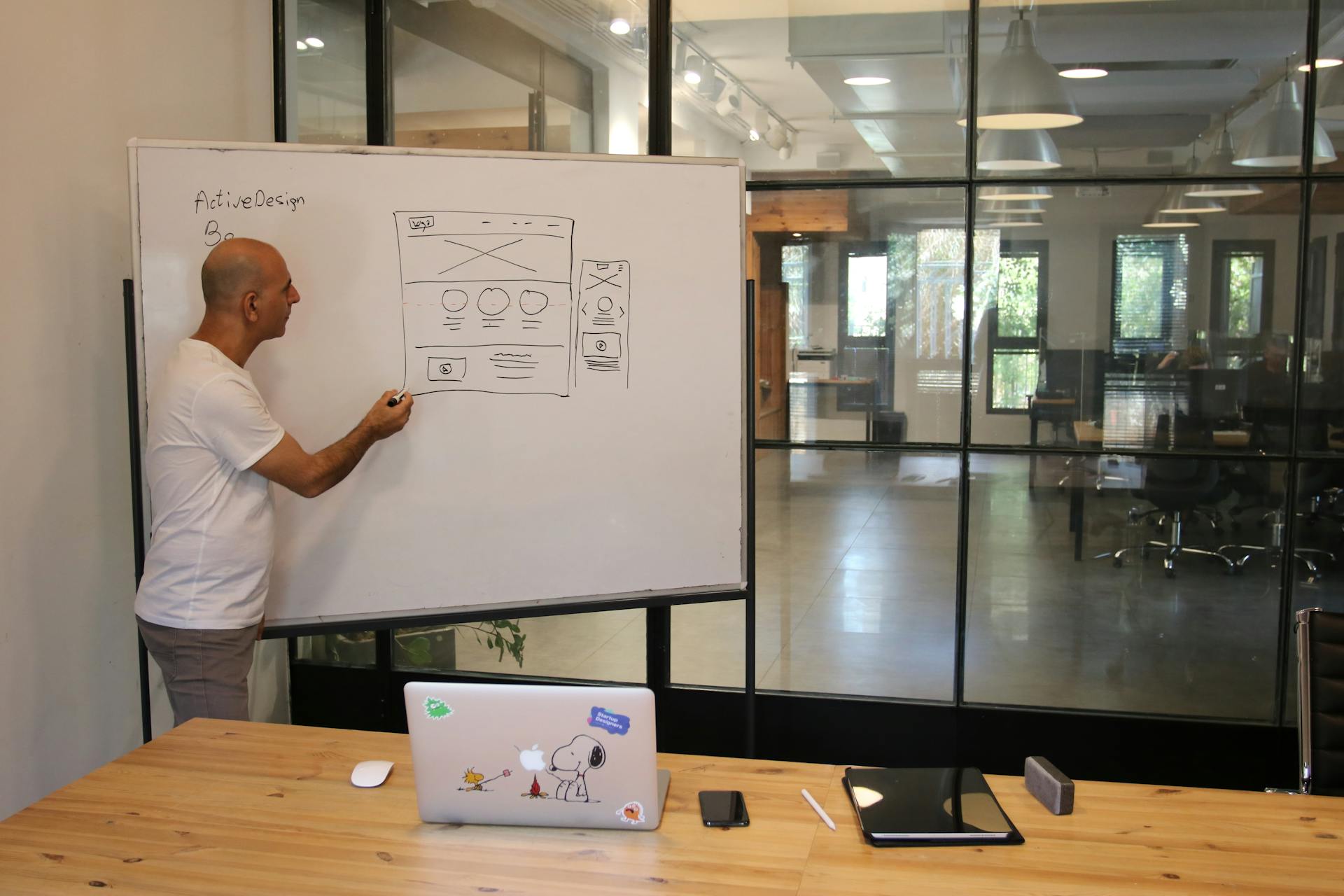 A focused designer in an office sketching a website layout on a whiteboard during a presentation.