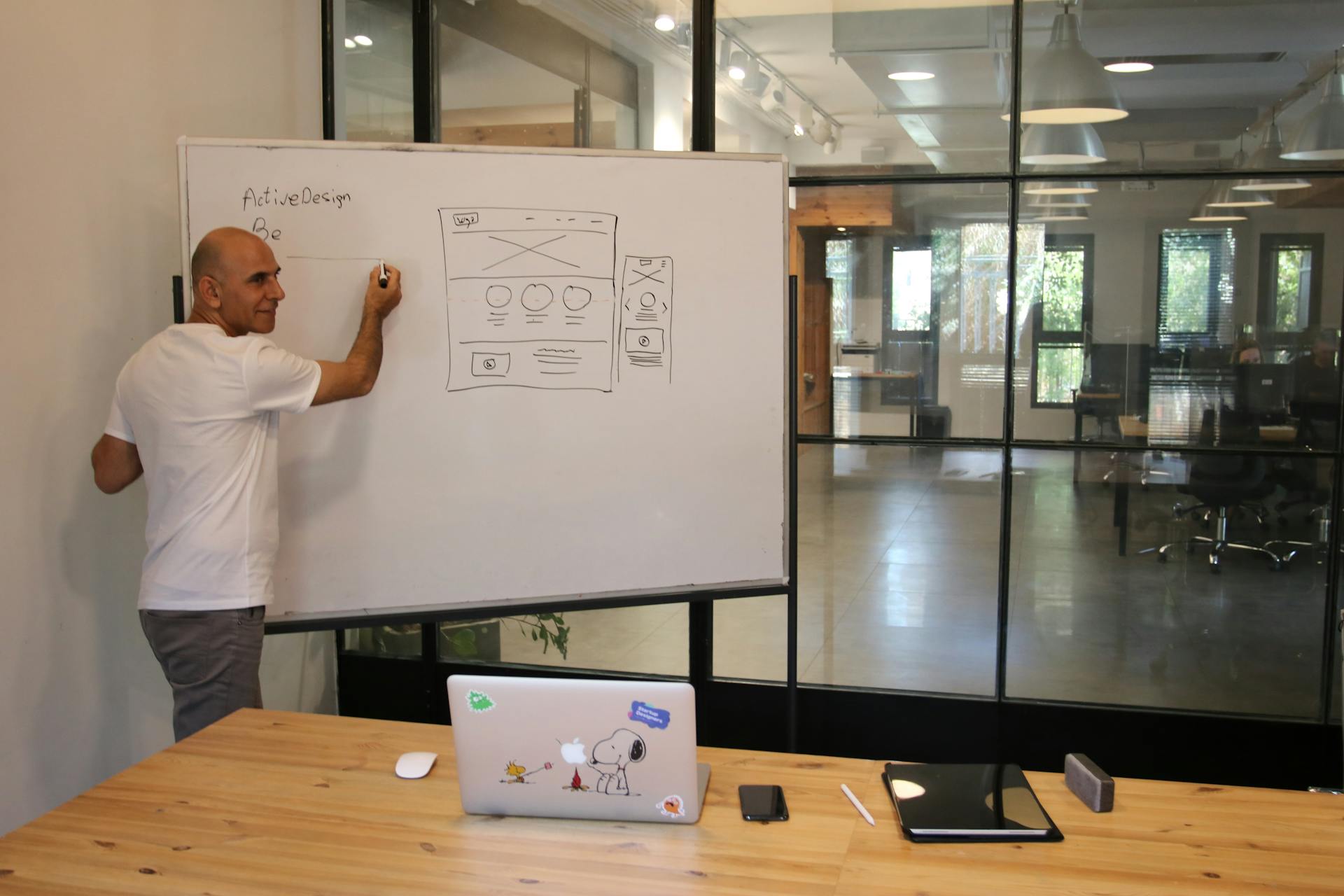 A man explaining a web design concept on a whiteboard in a modern office setting.