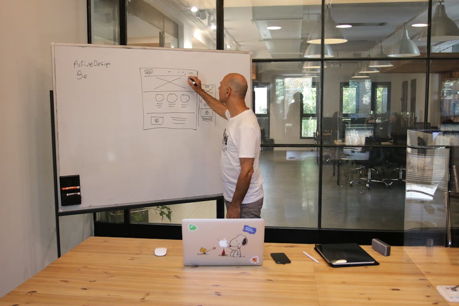 Side view of anonymous hairless male employee in white t shirt drawing draft on whiteboard while working on startup strategy in contemporary office