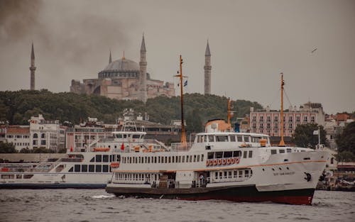 Various vessels floating on Bosporus near ancient buildings and famous Church of Hagia Sophia against cloudy sky