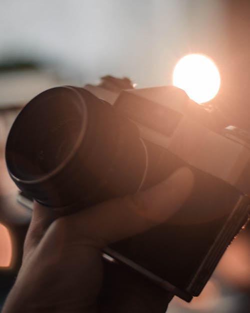 Crop faceless person holding vintage photo camera while shooting pictures against blurred background of illuminated street