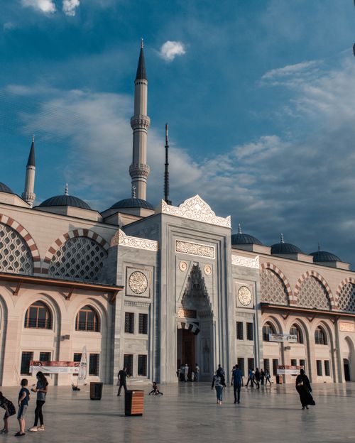 Free From below of amazing stone mosque with huge entrance and majestic ornament with people walking on square in cloudy day Stock Photo